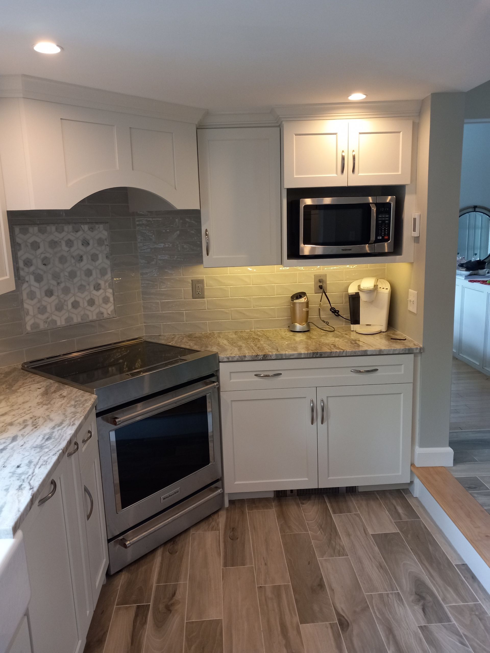 A kitchen with white cabinets, a stove, a microwave, and a coffee maker.