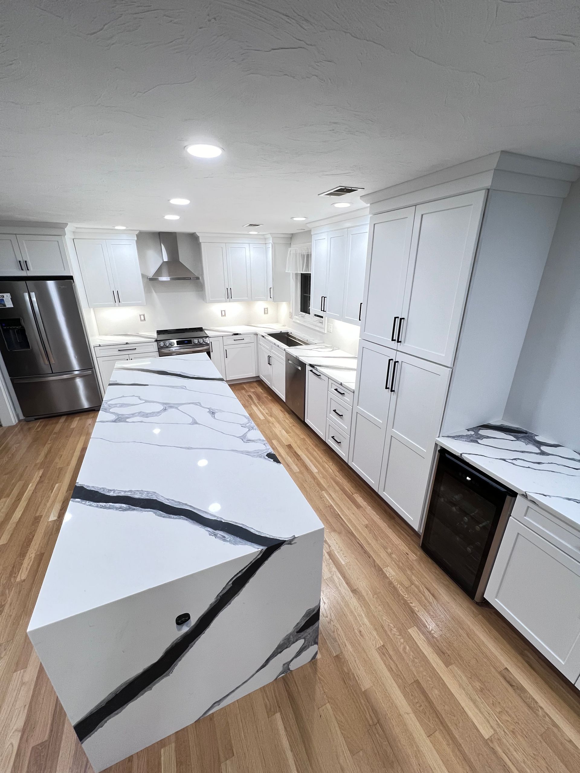 A kitchen with white cabinets and stainless steel appliances and a large island in the middle.