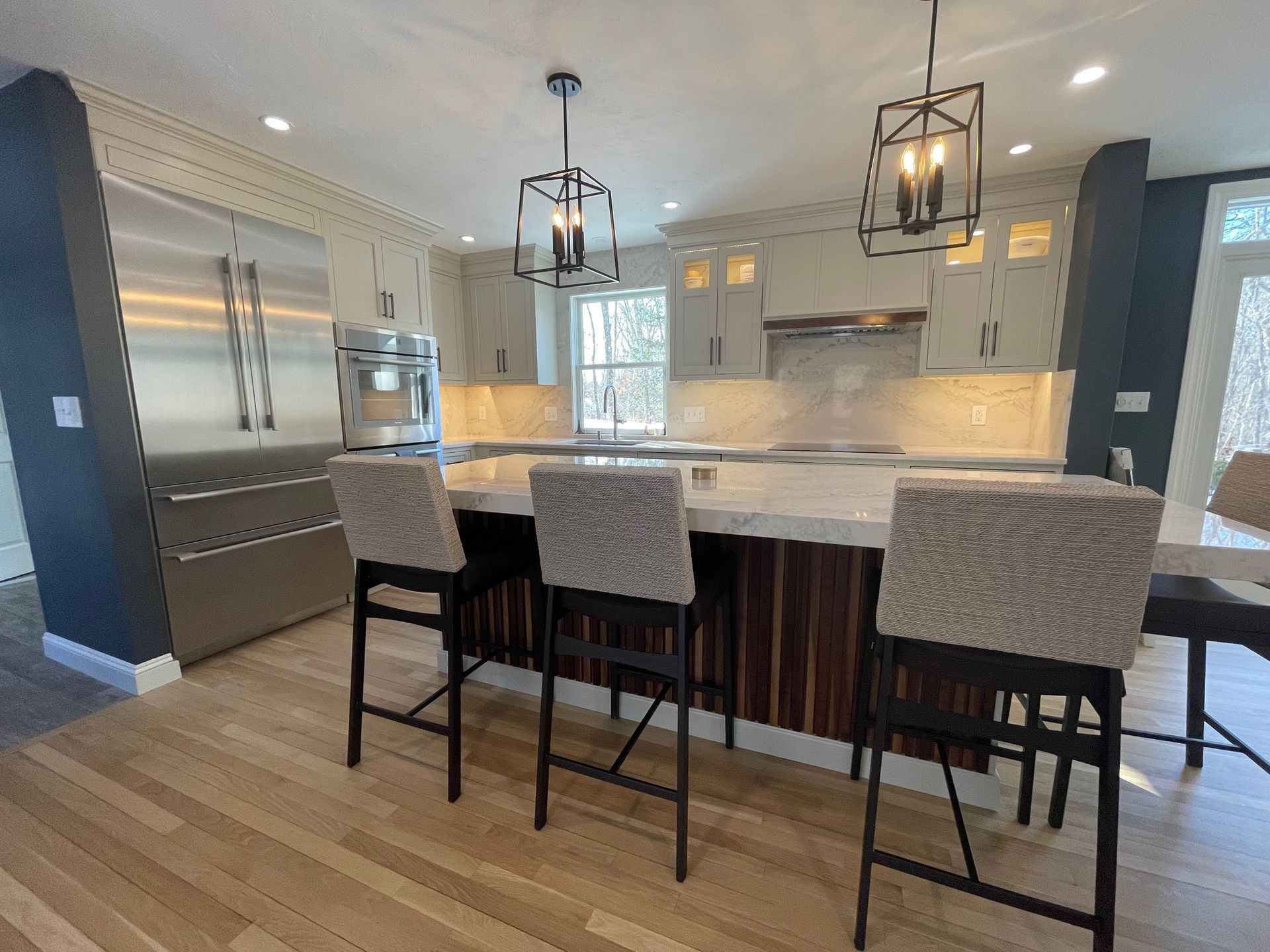 Modern kitchen with island, pendant lights, stainless steel appliances, and bar stools.