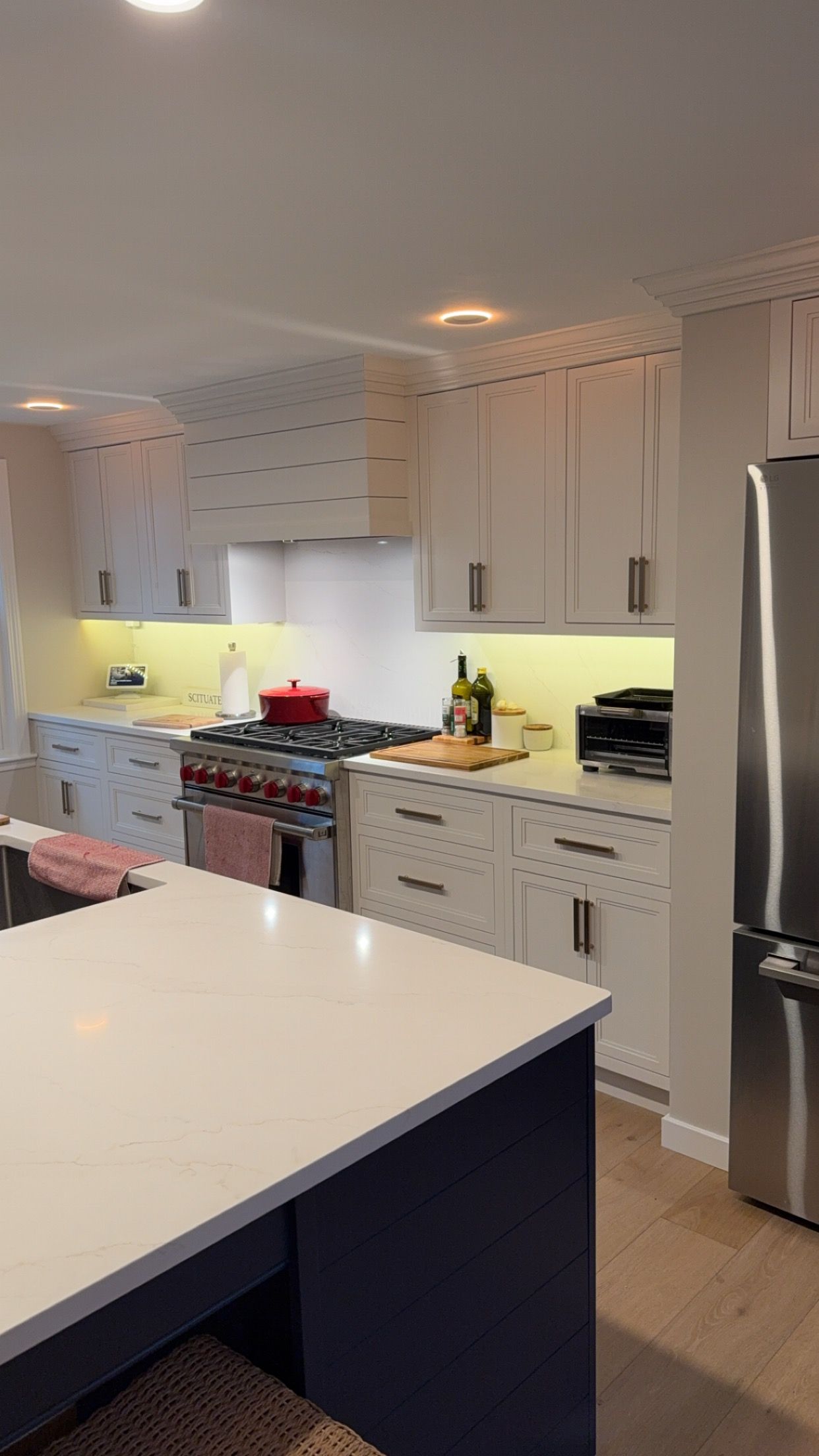 Bright white kitchen with stainless steel fridge, navy island, and a stove below white cabinets.
