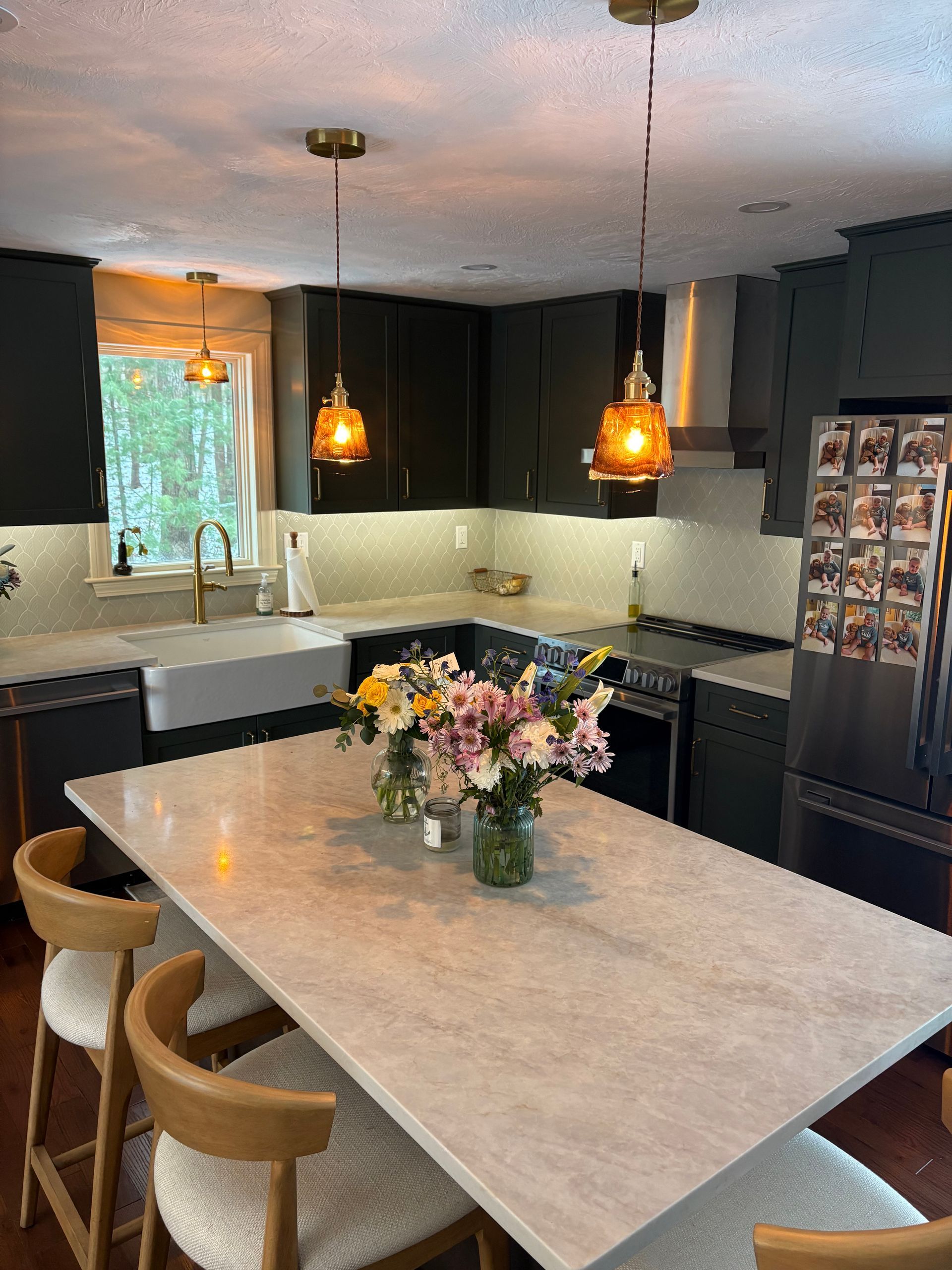 Modern kitchen with a large island, pendant lights, dark cabinets, and a vase of flowers on the counter