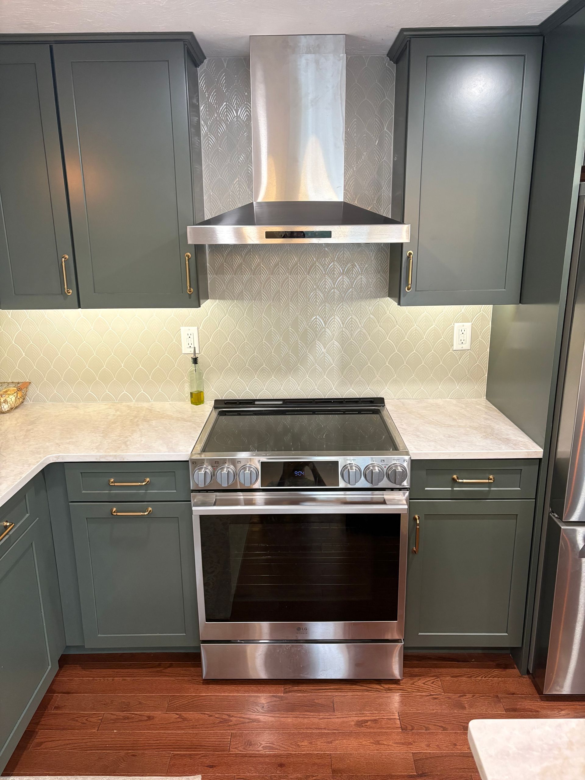 Modern kitchen with dark green cabinets, stainless steel range hood and stove, light countertops, and wood floor