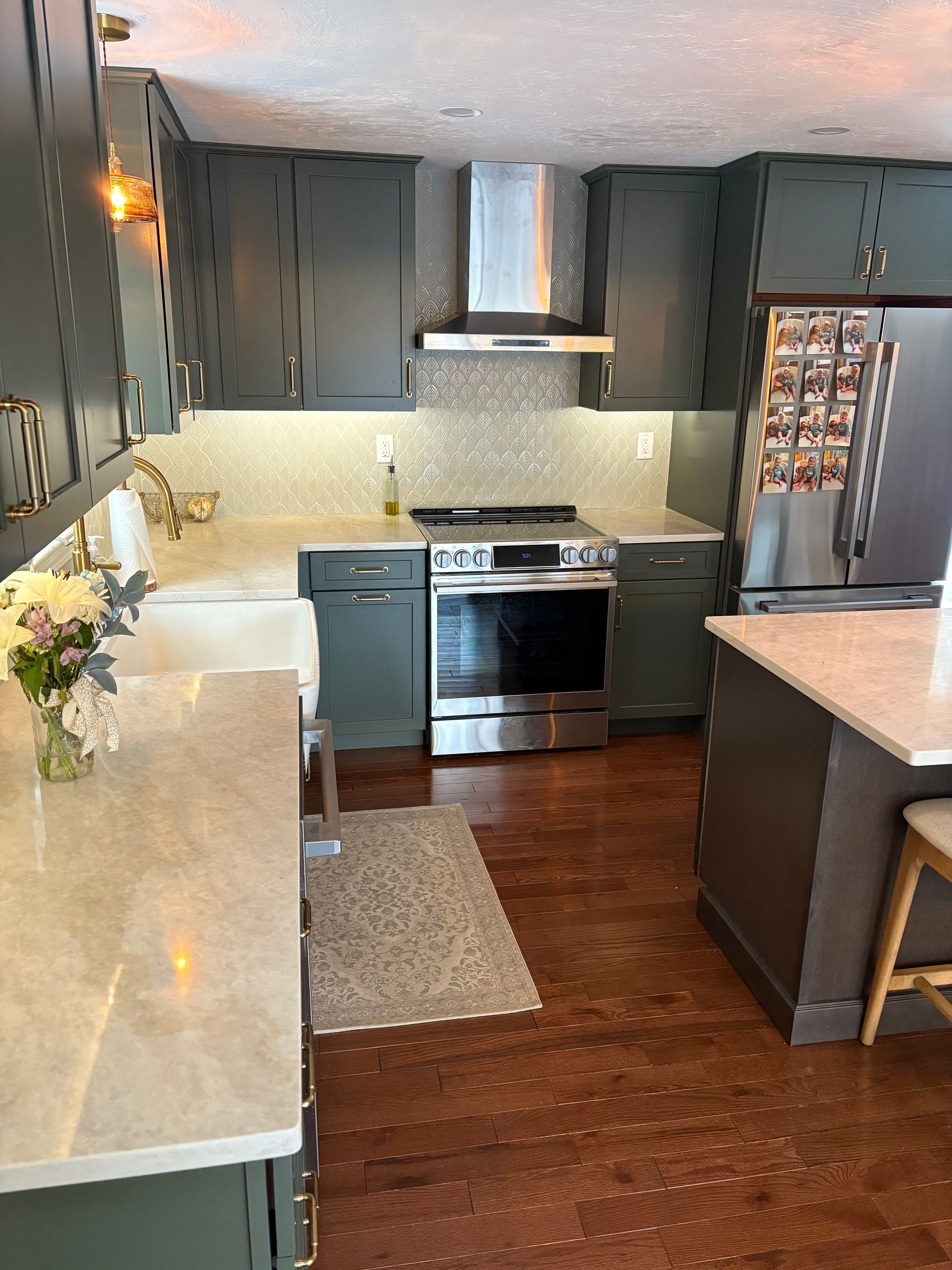 Modern kitchen with dark cabinets, stainless steel stove, white countertops, and a central island on wood floors