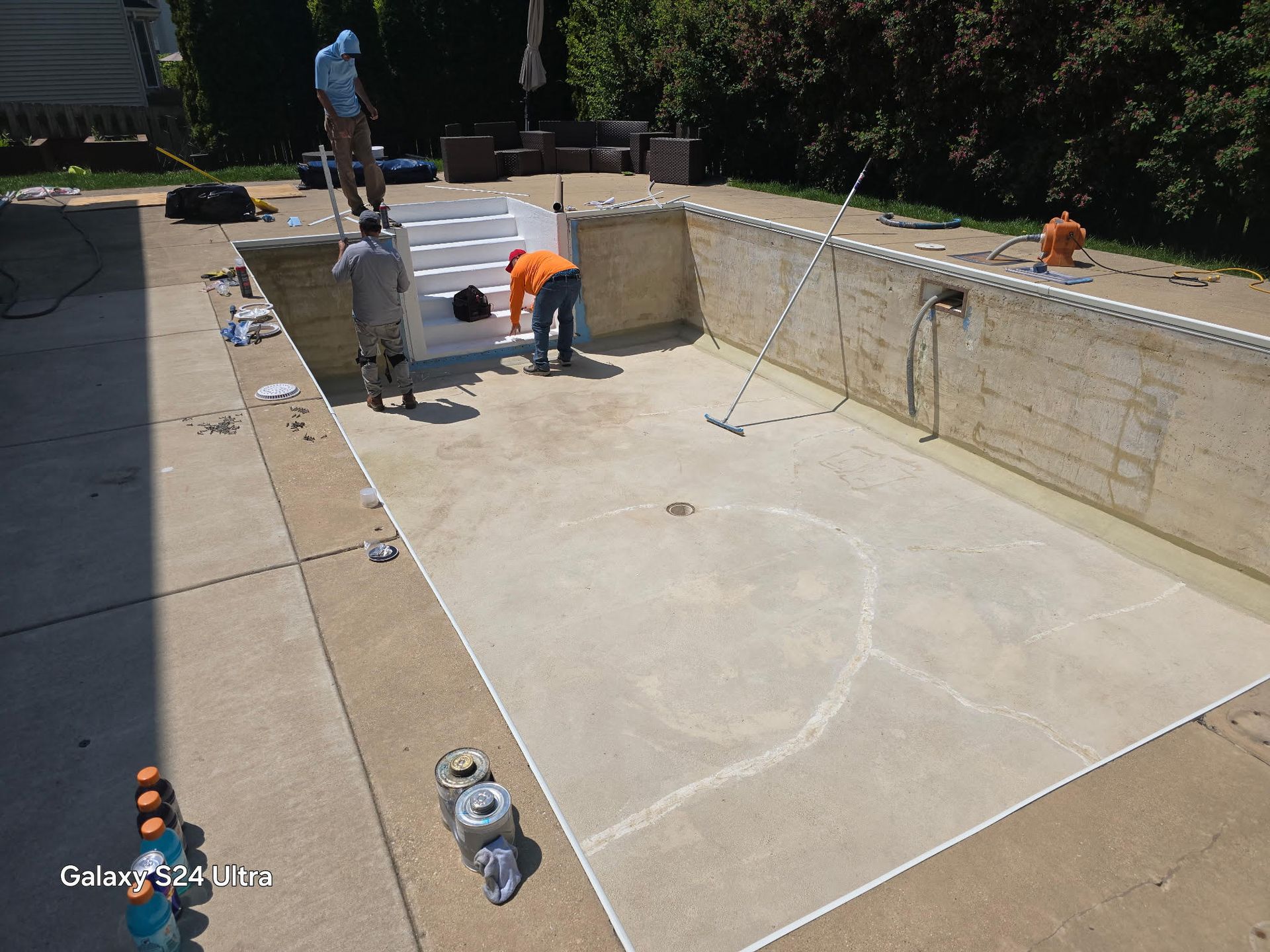 Workers install a new white liner in an empty rectangular backyard swimming pool on a sunny day.