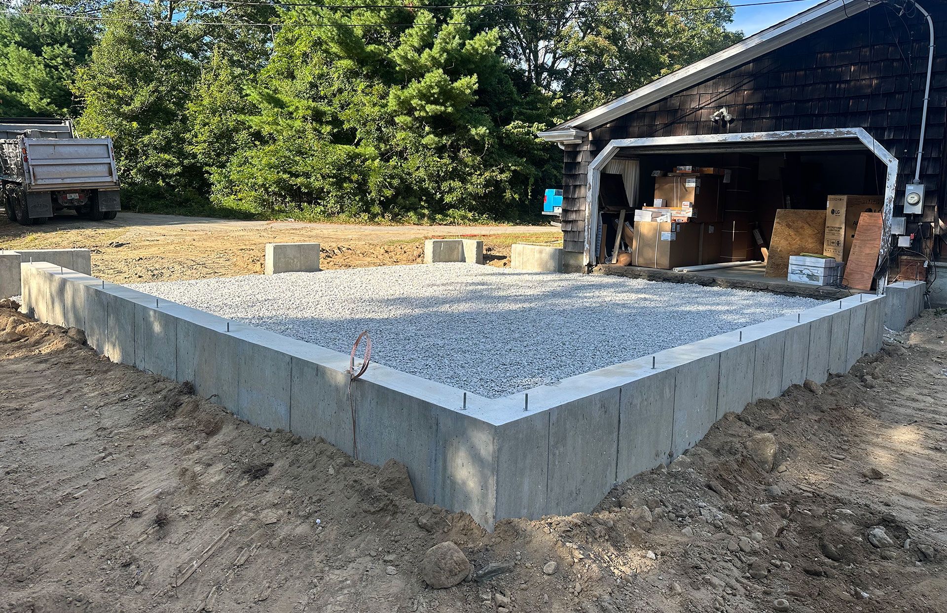 A newly poured concrete foundation filled with gravel for a building project next to a garage.
