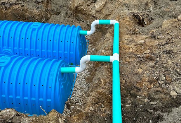 Two blue plastic septic chambers installed in a trench, connected by white pipes to a central green distribution line.