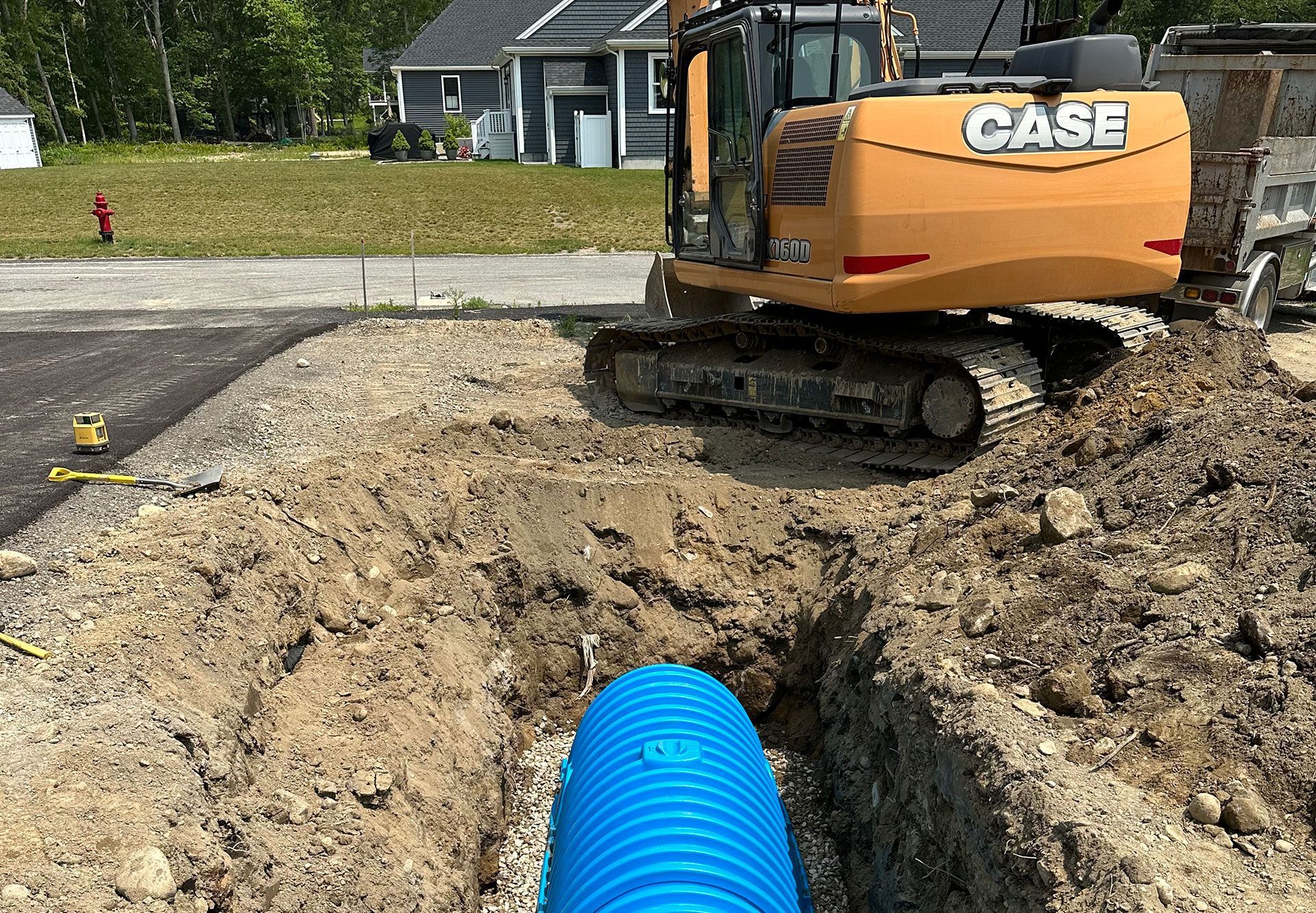 A blue drainage pipe installed in a trench at a construction site with a yellow CASE excavator parked nearby.