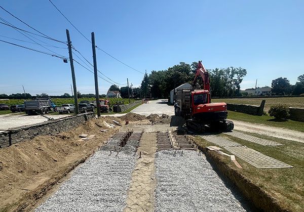 A red excavator sits on a dirt road undergoing construction, with gravel strips laid in the center of the path.