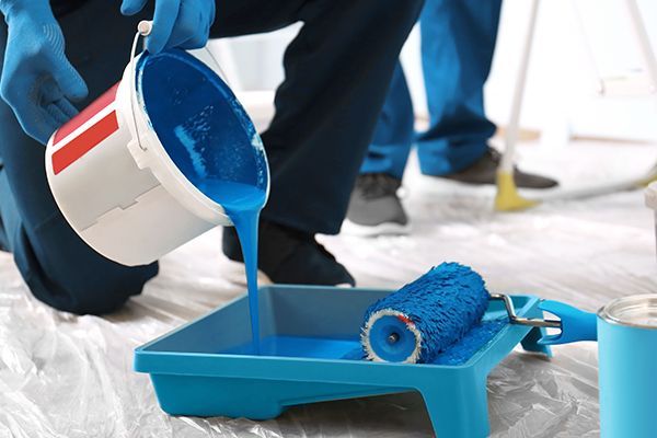 A person is pouring blue paint into a paint tray.