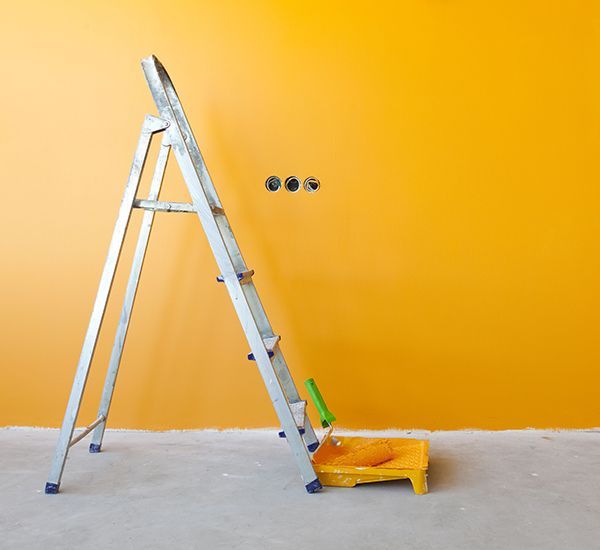 A ladder is sitting in front of a yellow wall.