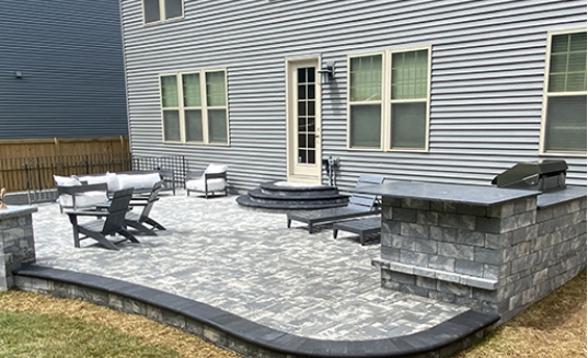 Curving wet stone walkway beside a green lawn and flower bed, reflecting sunlight