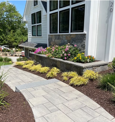 Front walkway of a white house with stone planter boxes and blooming flowers along the path