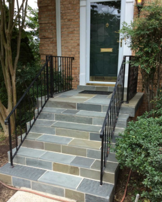 Front steps with slate tiles, black railings, and a green front door at a brick house entrance