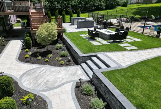 Landscaped patio with curved stone path, steps, black seating area, and green lawn near a building