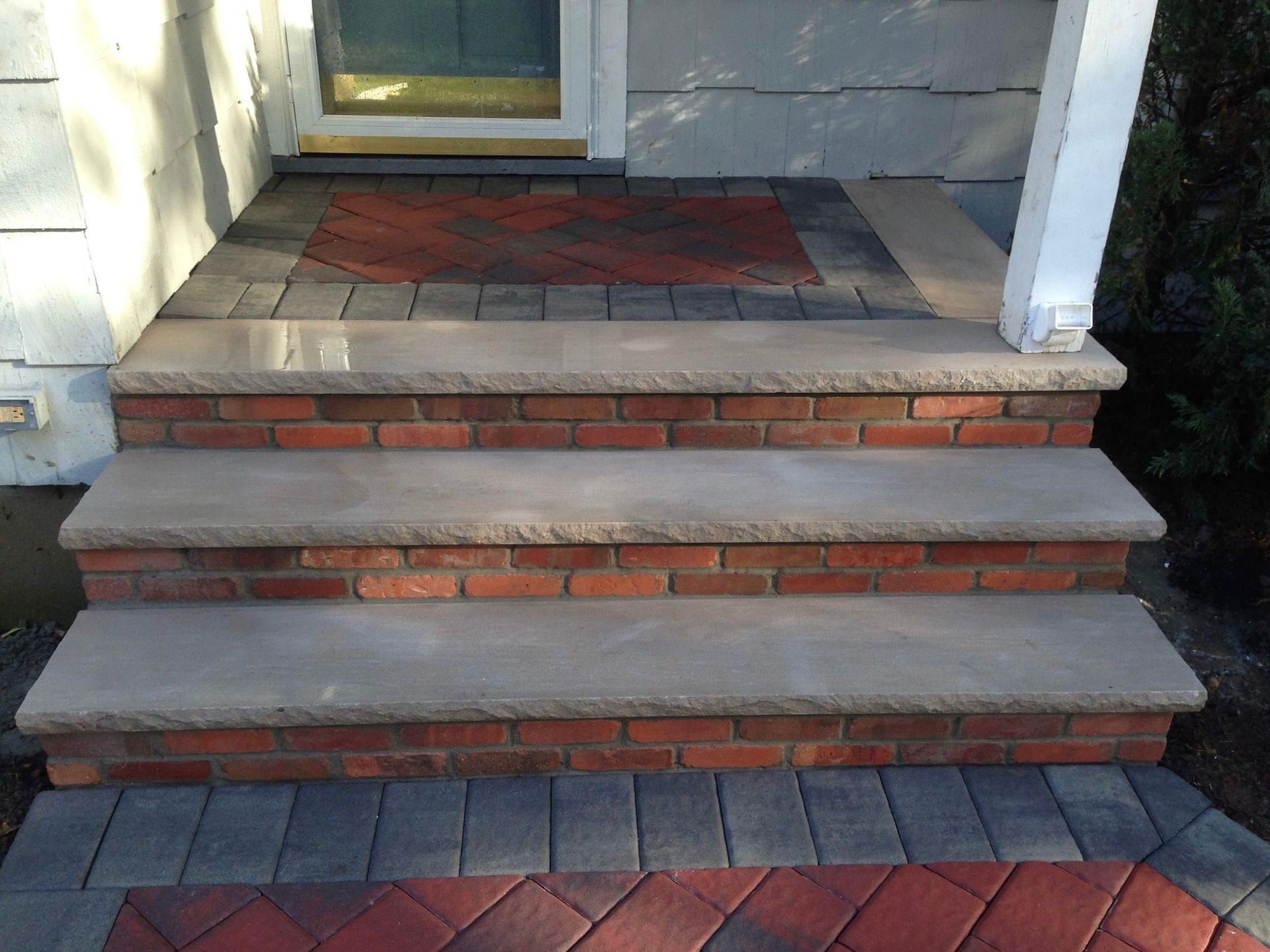 Brick steps leading to a doorway, bordered by pavers.