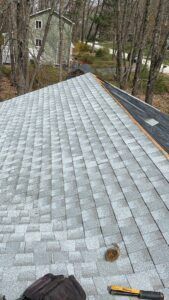 Gray asphalt shingles on a roof, tool bag and trees in the background.