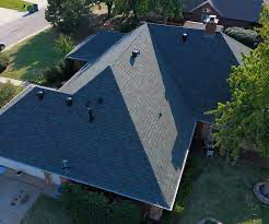 Aerial view of a dark blue shingled roof on a suburban home with several vents and a brick chimney.