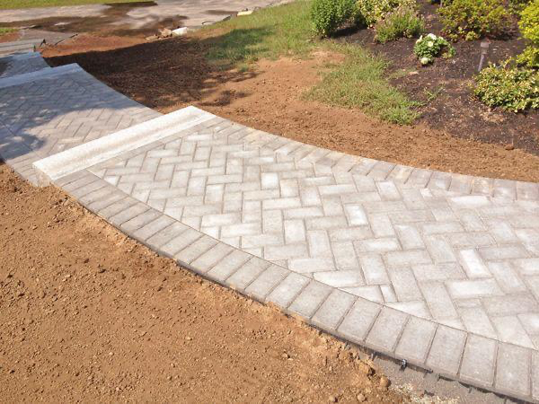 Brick pathway with steps, bordered by darker bricks, winding through a landscaped yard.