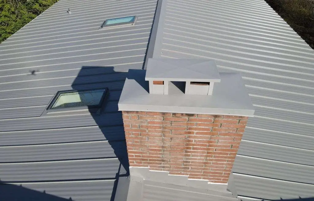 Gray metal roof with brick chimney and two skylights.