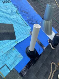 Roof construction with blue underlayment, a vent pipe, and a chimney base.