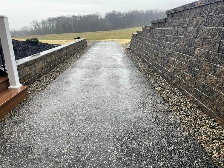 A brick wall along the side of a driveway leading to a field.