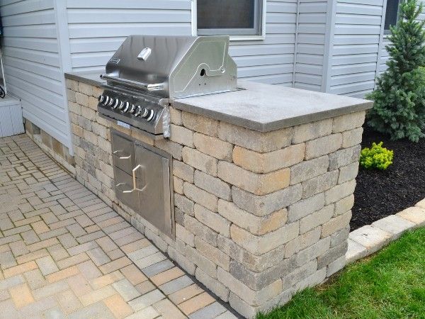 A grill is built into a stone wall next to a house.
