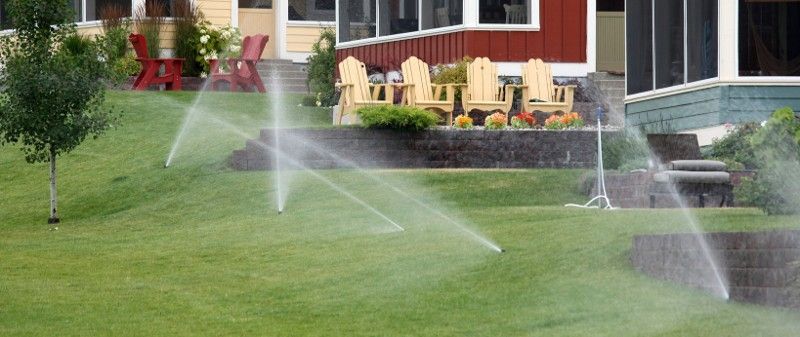A lawn with sprinklers spraying water on it in front of a house.