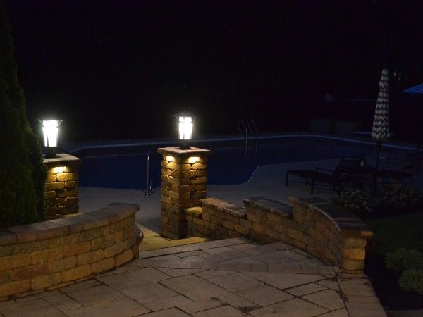 A brick walkway leading to a swimming pool at night