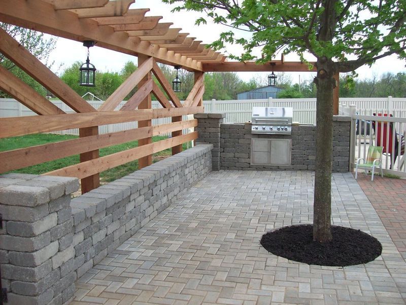 A brick patio with a grill under a wooden pergola