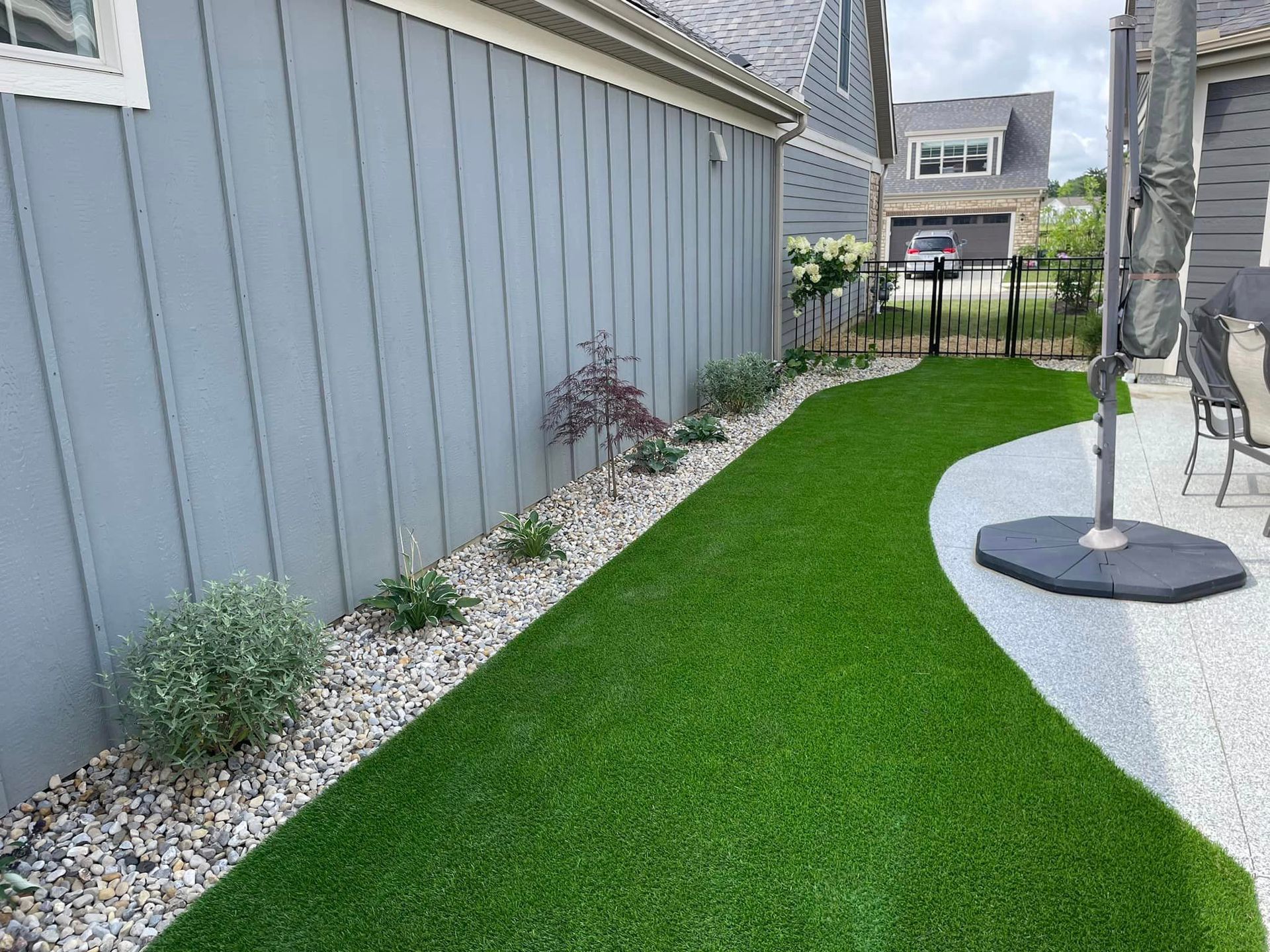 A lawn with a patio and umbrella in the backyard of a house.