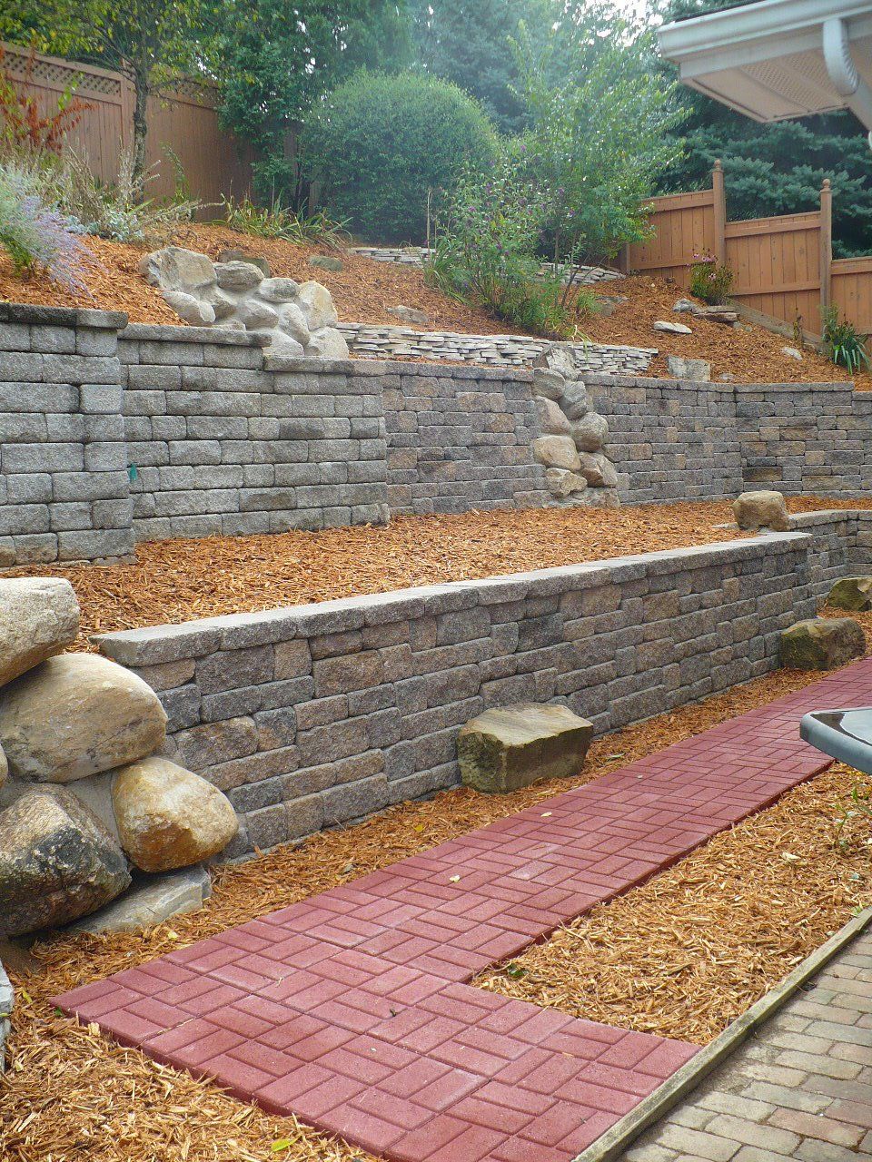 A brick wall is sitting on top of a hill next to a red brick walkway.