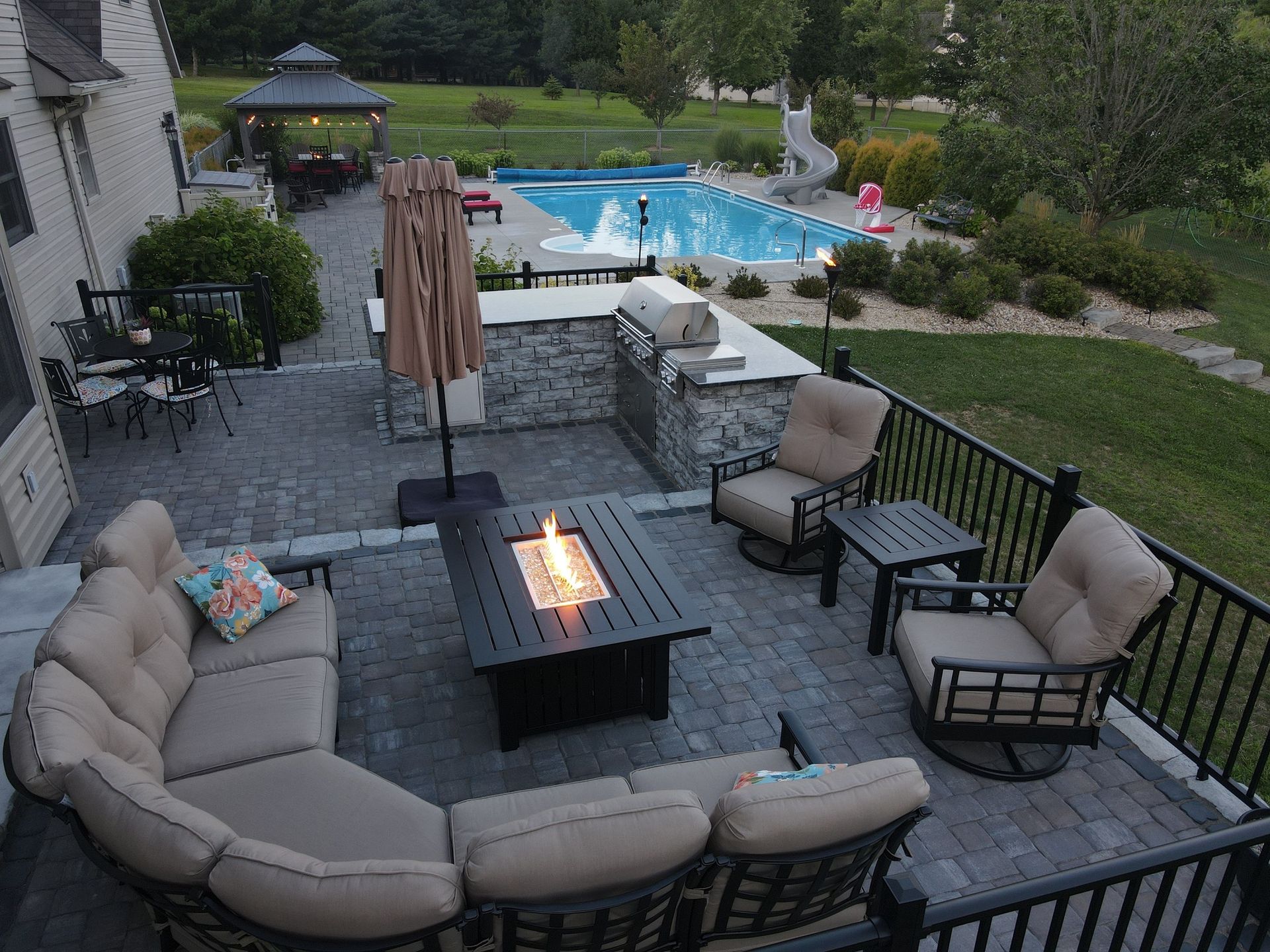 A patio with a fire pit and a swimming pool in the background