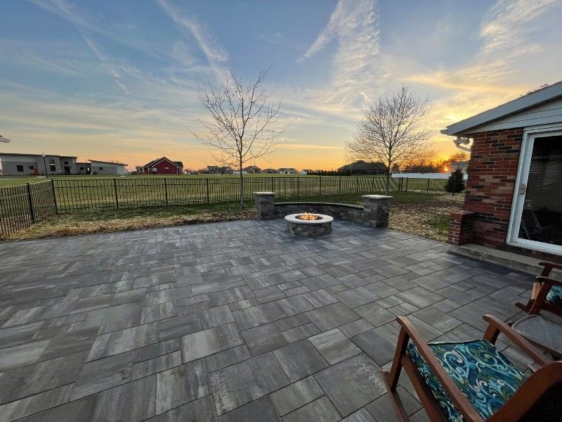 A patio with a fire pit and chairs in front of a house at sunset.