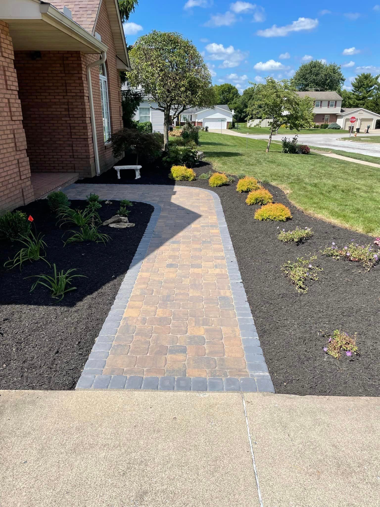 A brick walkway leading to a house with a bench in the middle of it.