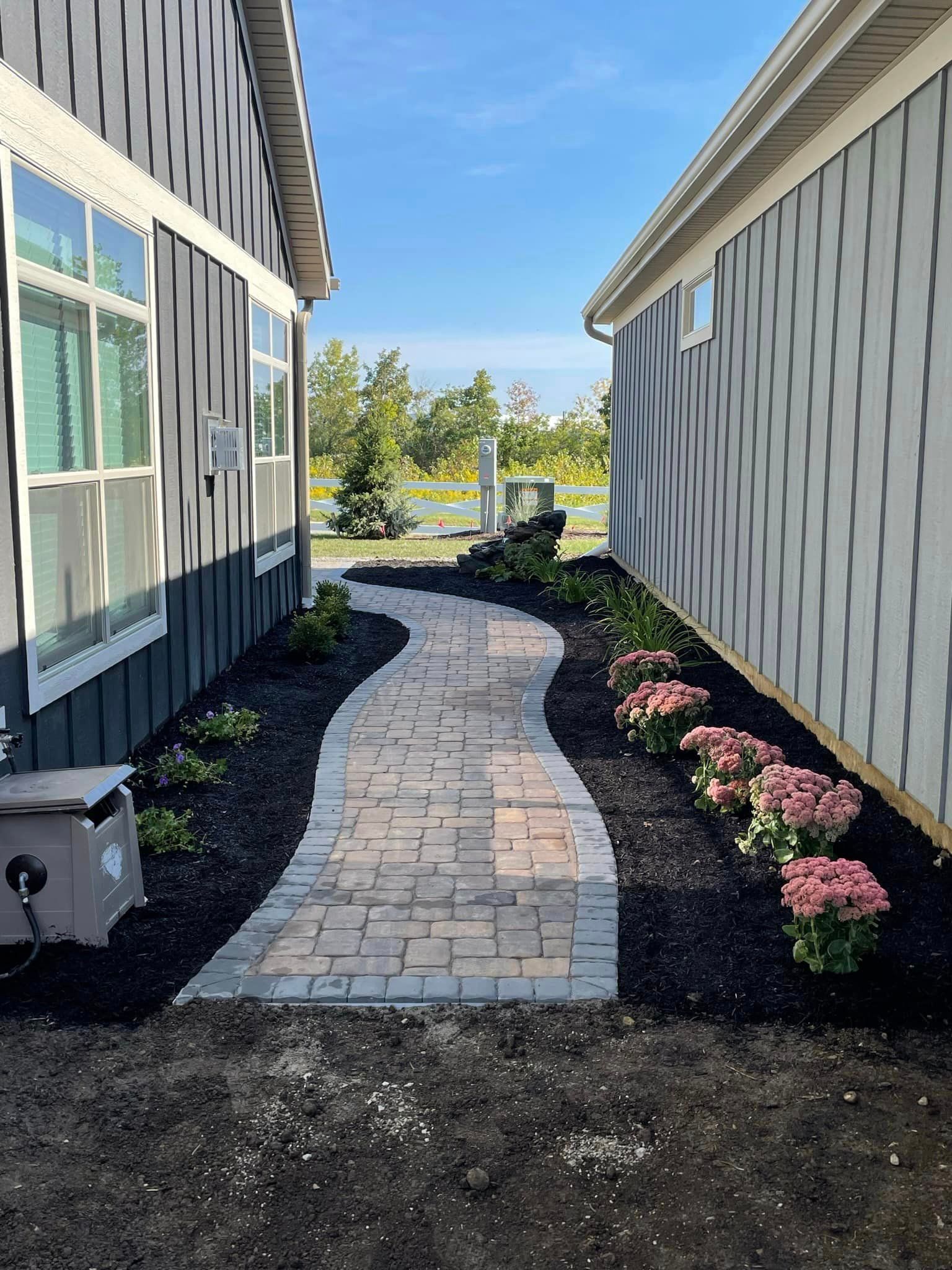 A walkway between two houses with flowers on the side.