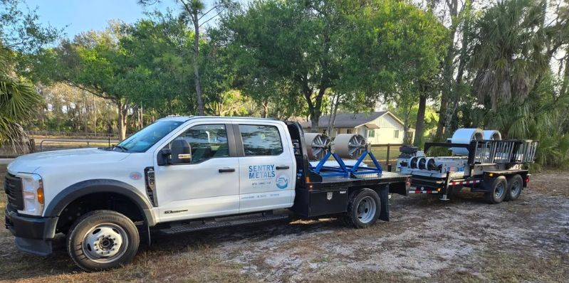 White pickup truck towing a trailer with equipment and a small vehicle on a muddy road near trees