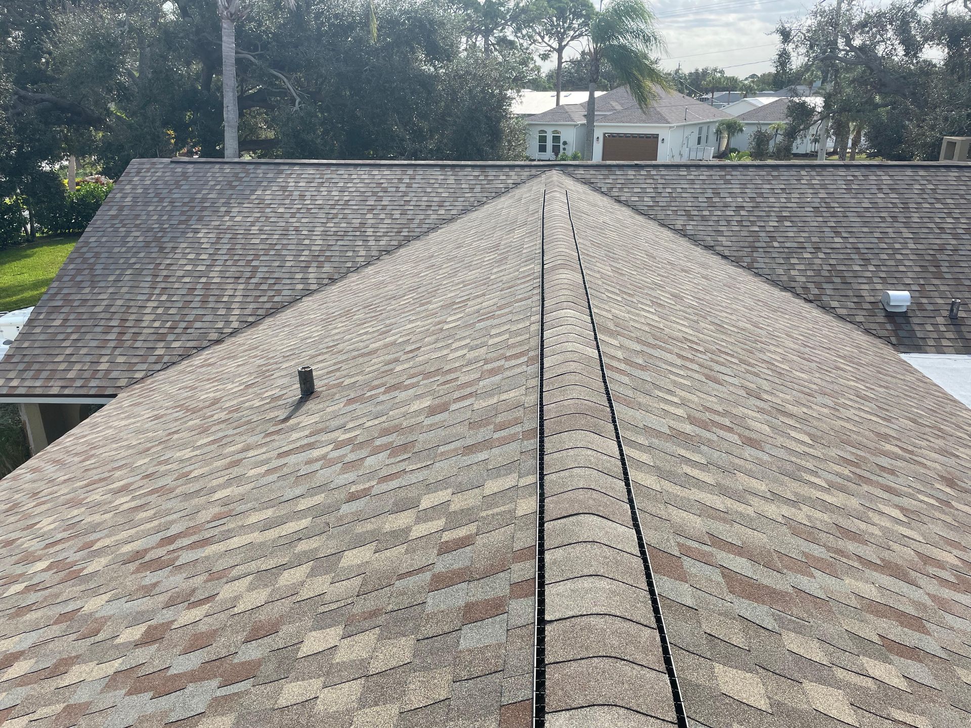 View of a roof with asphalt shingles, tan, brown, and grey, on a sunny day.