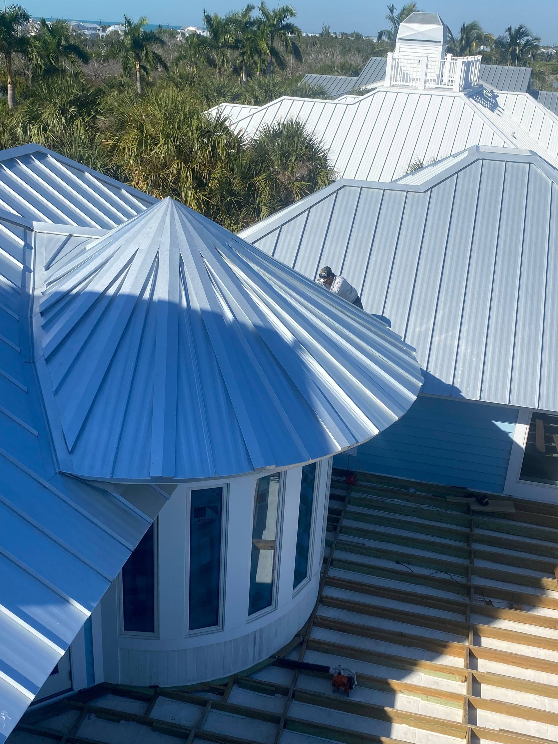 Metal roofs of a building in bright sunlight with surrounding trees in background.