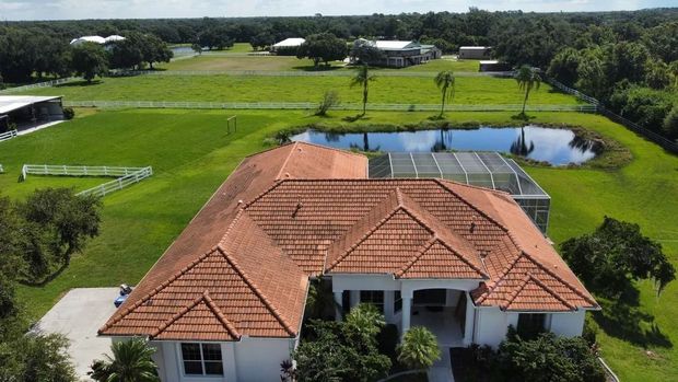 Aerial view of a white house with a terracotta tile roof, set on green acreage, with a pond.