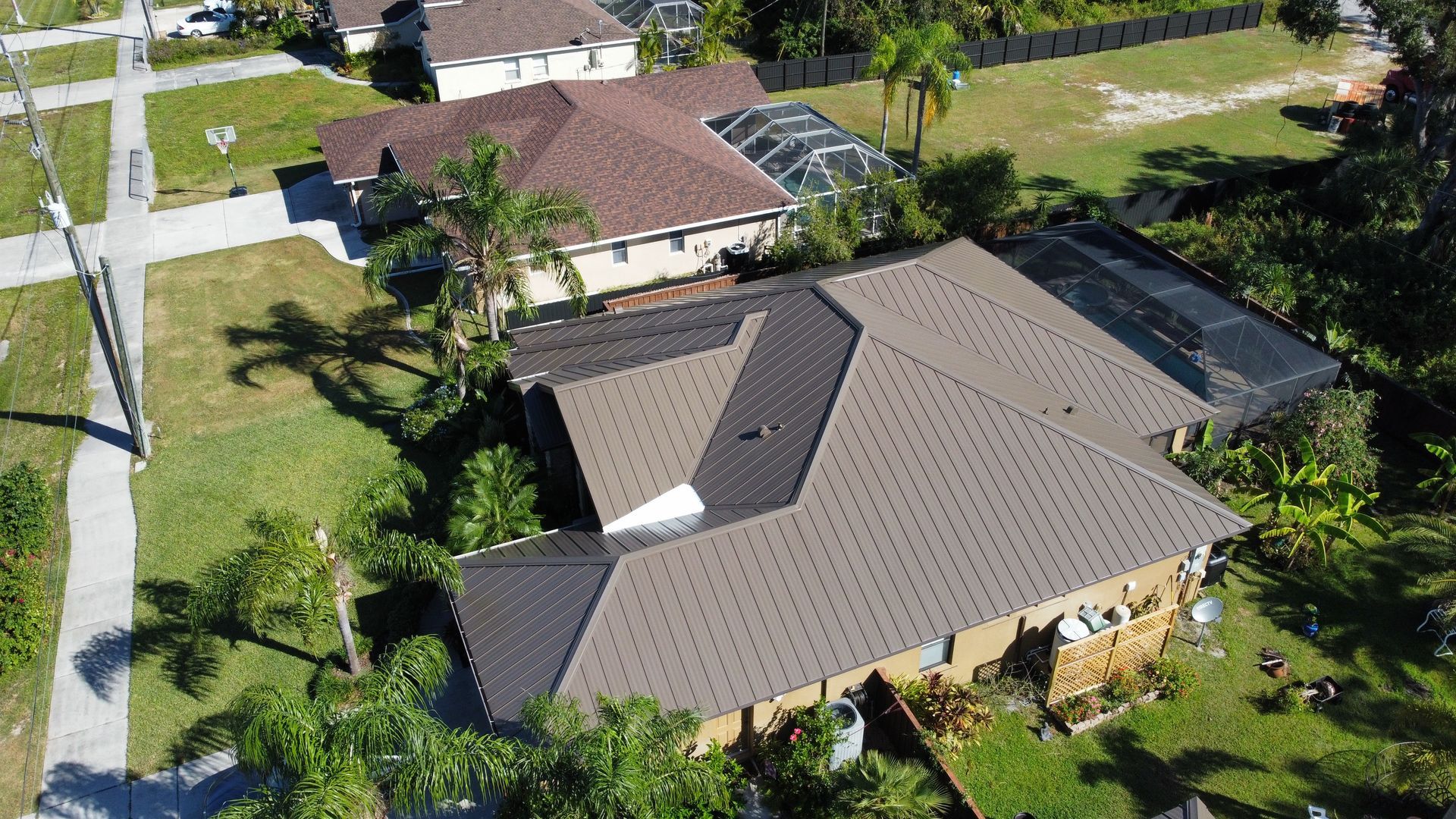 Aerial view of homes with brown roofs and green lawns in a sunny neighborhood.