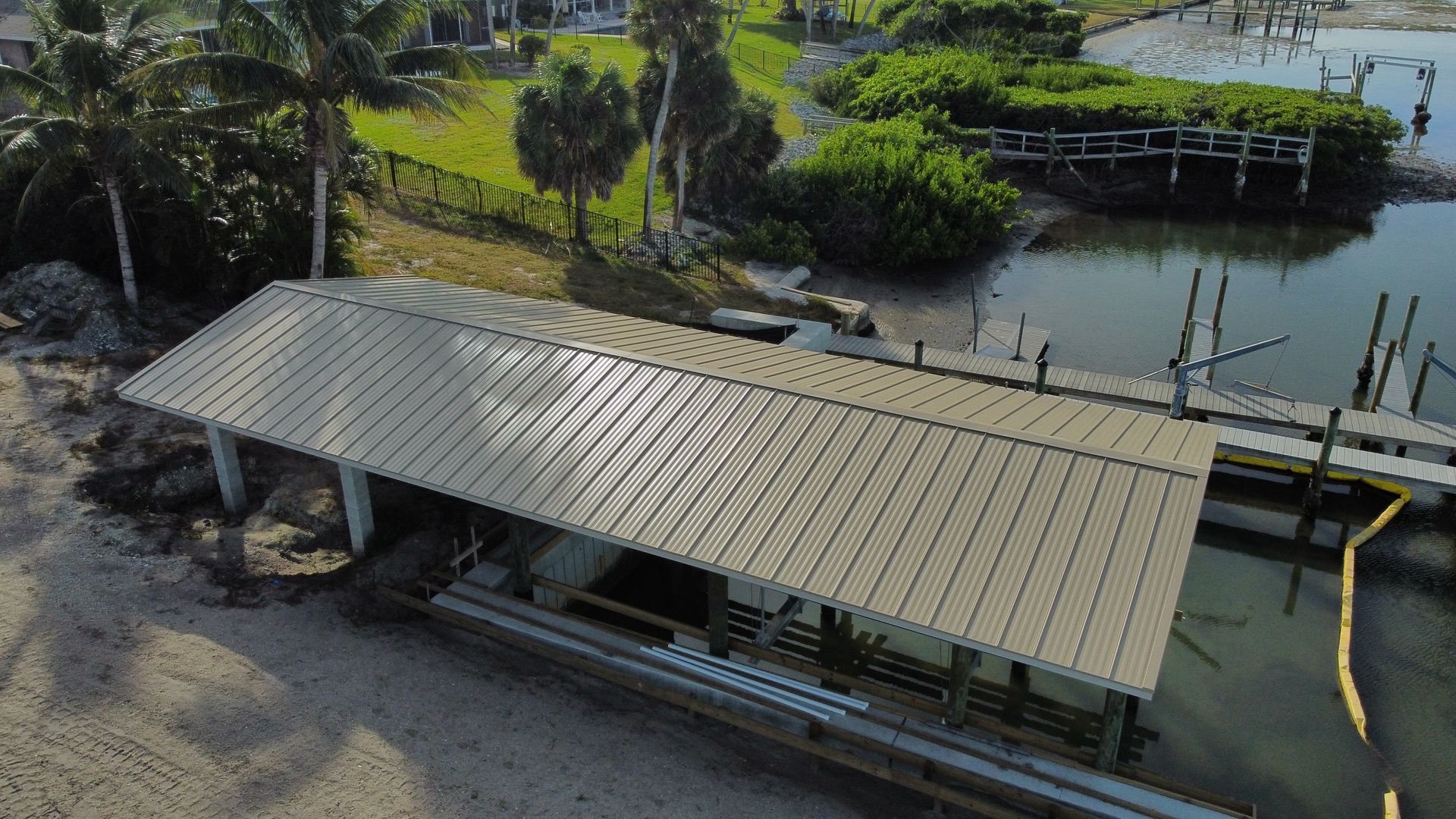 Overhead view of a boat dock with a metal roof. A waterway is in the background with green vegetation and a house.