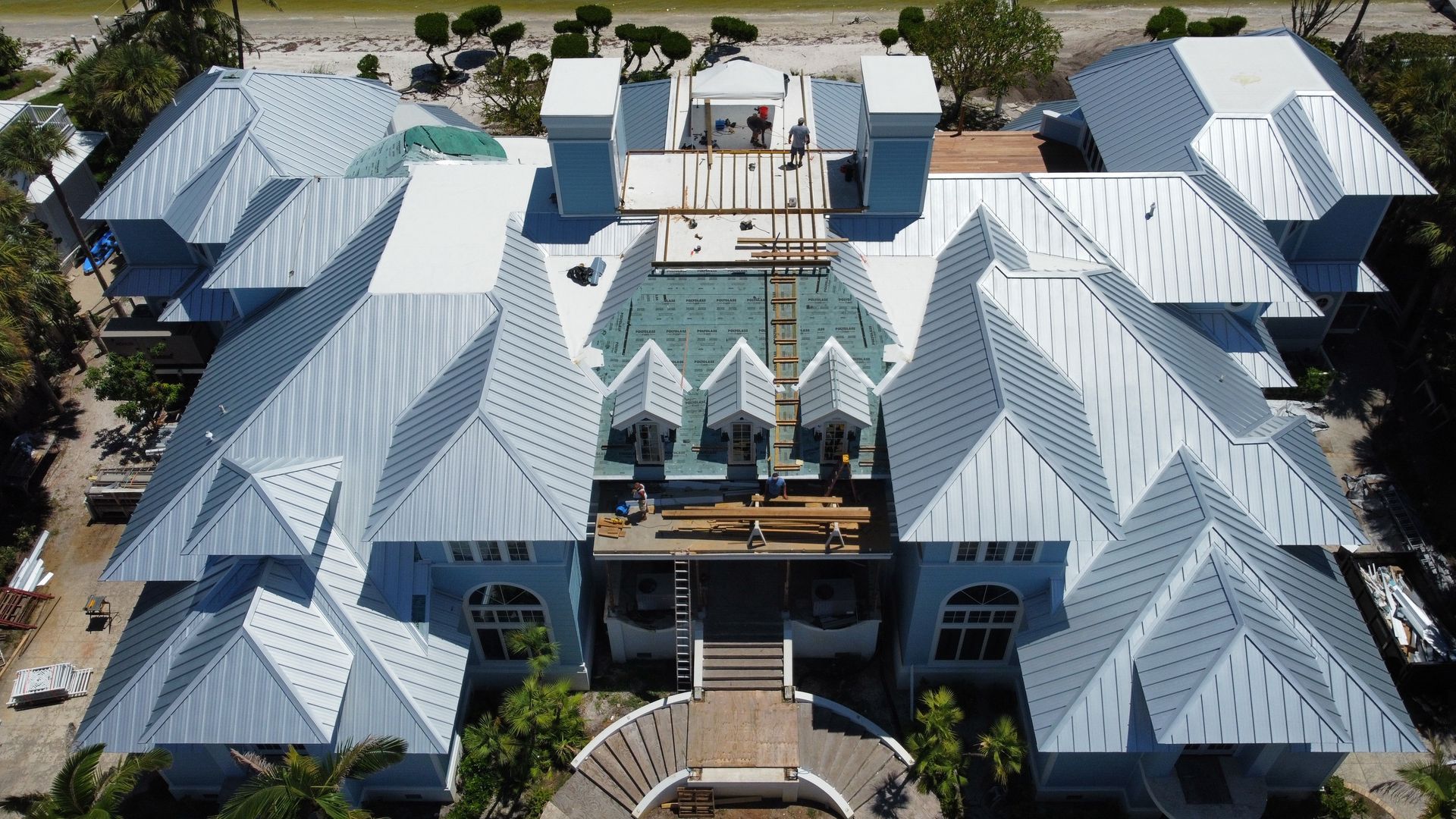 Aerial view of large, light blue house with multiple peaked silver roofs.