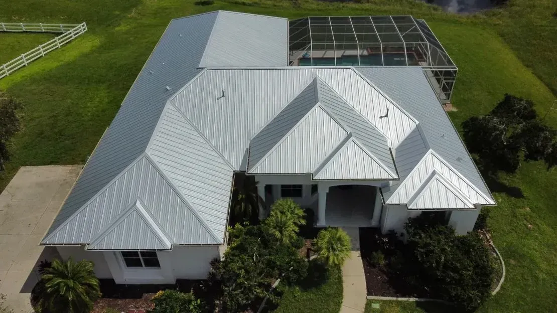 Aerial view of a white house with a gray metal roof, surrounded by green grass.