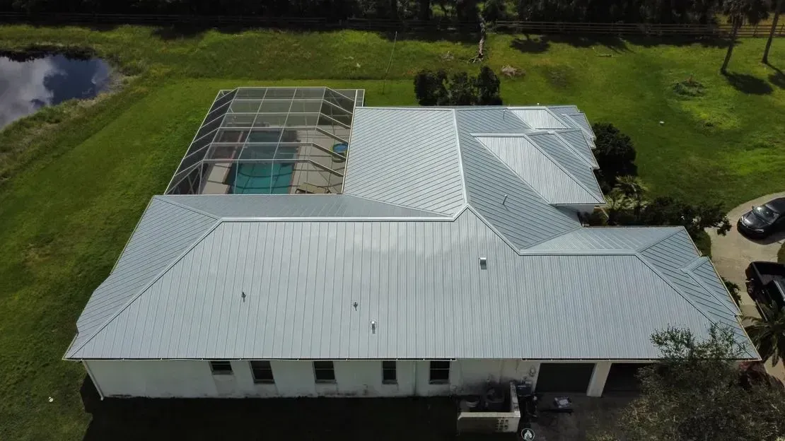 Aerial view of a white house with a metal roof, a pool, and green lawn.