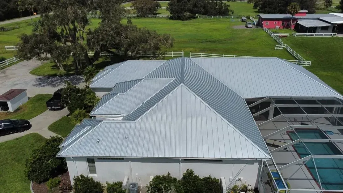 Aerial view of a house with a silver metal roof, a pool, and surrounding green grass.