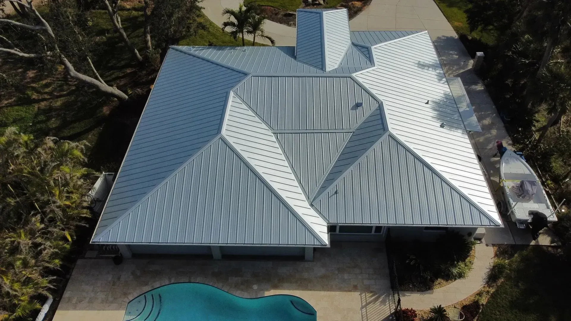 Aerial view of a house with a complex silver metal roof, chimney, and a swimming pool.