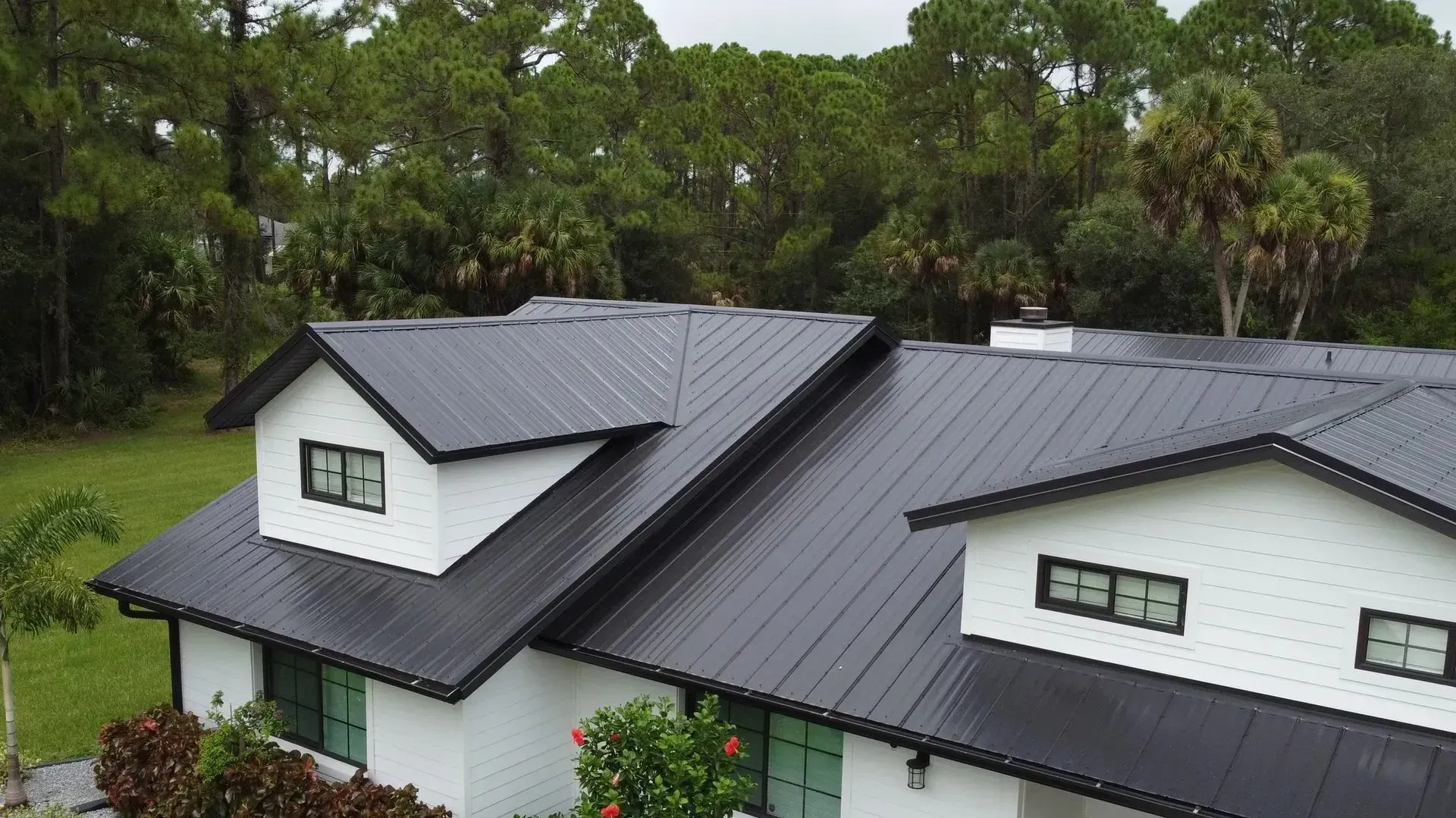 Black metal roof on a white house with black trim, surrounded by green trees.