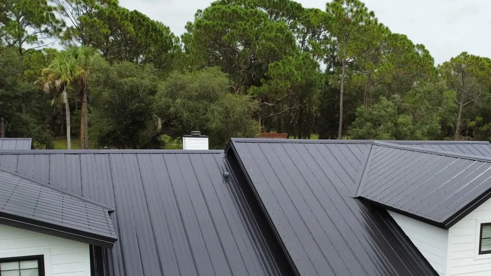 Black metal roof on a white house, with trees in the background.