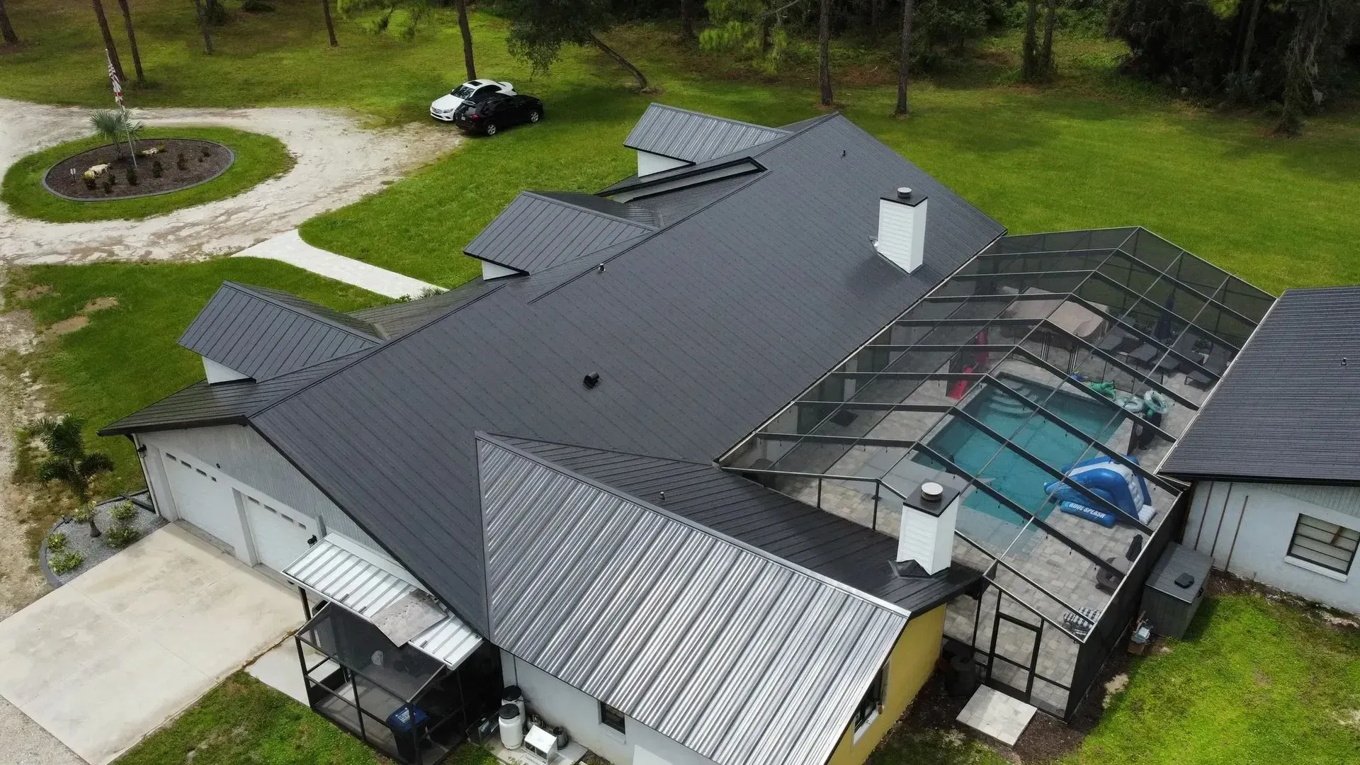 Aerial view of a dark metal roof house with a screened-in pool and driveway.