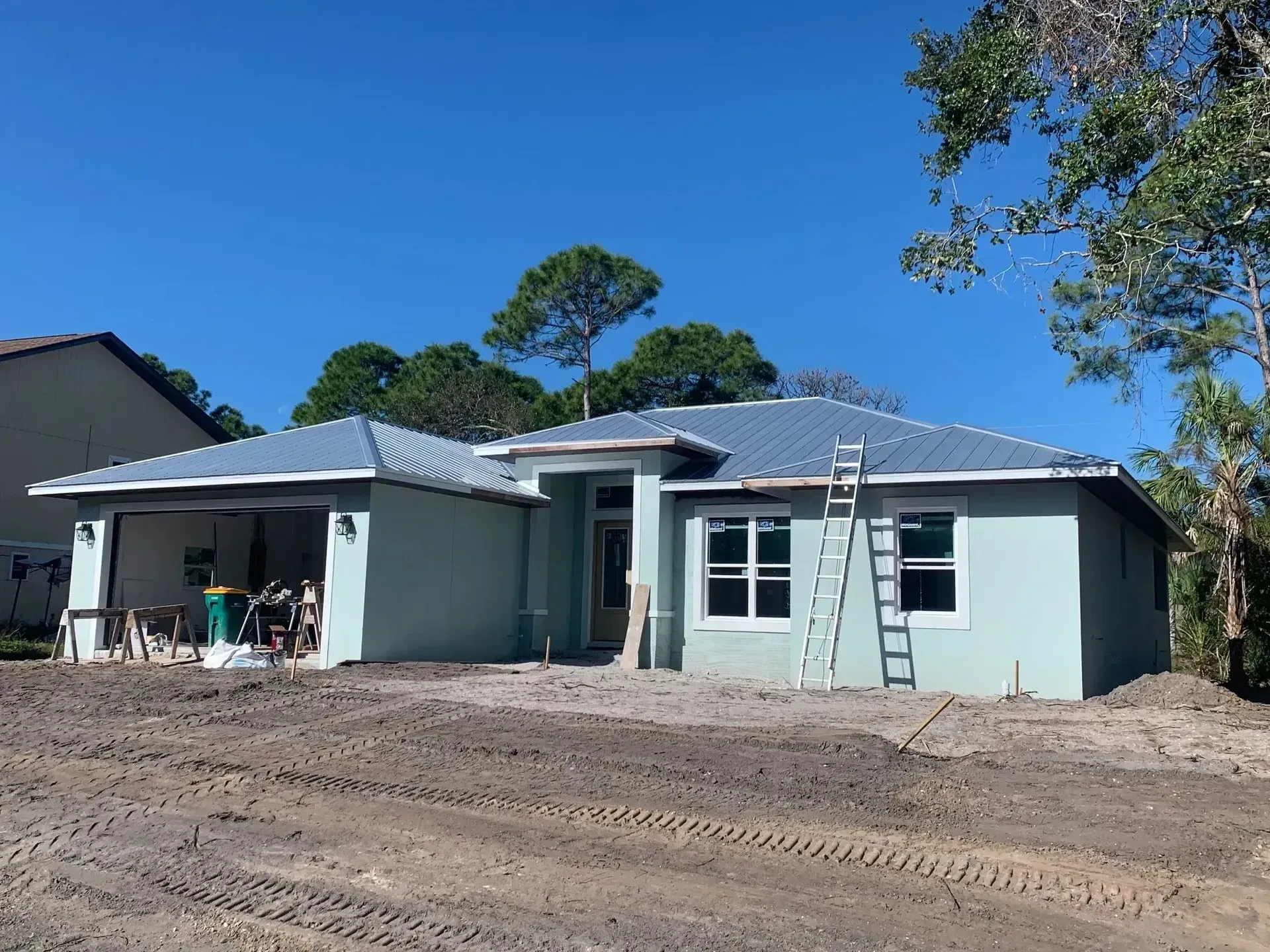 Light blue house under construction with a metal roof on a sunny day.